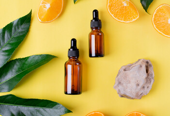 Serum bottles, orange fruit, palm leaf and stone on yellow background. Flat lay. Skincare product...