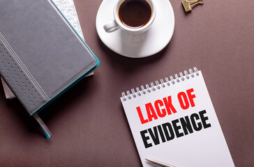 On a brown background, diaries, a white cup of coffee and a notebook with LACK OF EVIDENCE