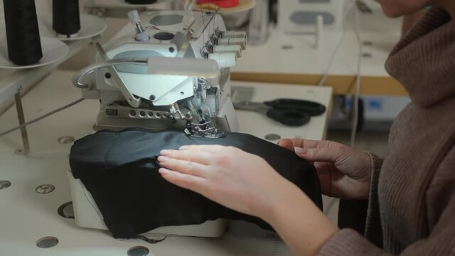 Sewing workshop. Processing the edge of the product on the overlock. Zigzag machine stitch. Fabric lining. A woman sewing on an industrial sewing machine. Hands close-up. Overlock