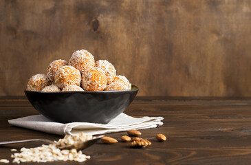 Homemade energy balls of raw carrots, dried fruits, oatmeal and nuts in a brown bowl on a wooden background.