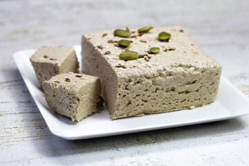 Halva close-up on a white plate on a white wooden background. Traditional oriental dessert sweet halva. Halva made from sunflower seeds. side view, copyspace.