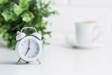 White retro alarm clock, flowers and a cup of coffee on the background of a white brick wall. The...