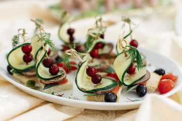Snack for a banquet or buffet. Skewered canapes of fresh cucumber, meat and tomato, decorated with berries and herbs, a feast.