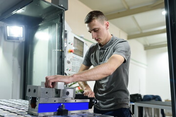 a man puts an aluminum piece on a cnc machine and prepares a processing machine..