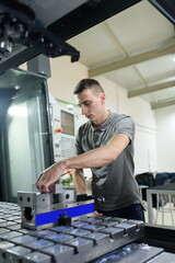 a man puts an aluminum piece on a cnc machine and prepares a processing machine..
