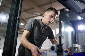 a man puts an aluminum piece on a cnc machine and prepares a processing machine..