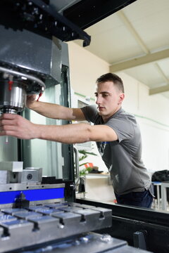 a man puts an aluminum piece on a cnc machine and prepares a processing machine..