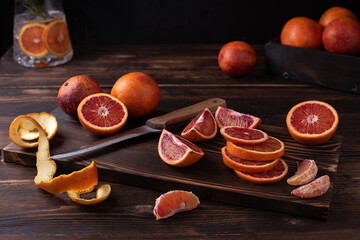 Sliced and halved blood oranges on a cutting board on a dark wooden background, healthy food,...