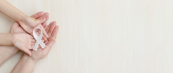 A white ribbon in the hands of a child and a mother or grandmother on a white background.Concept lung cancer awareness November month. Top view. Copyspace