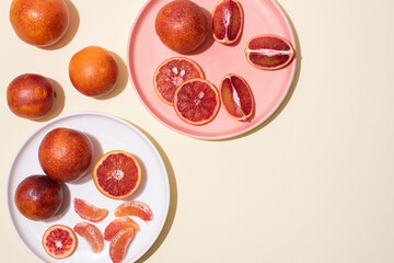 Plates with whole and sliced blood oranges on yellow background in bright light, top view.