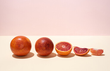 A row of whole and cut into halves and slices of bloody oranges on a yellow-pink background in...