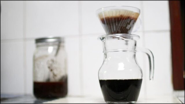 Cold Brew drip brewing; clear glass of coffee jar and paper dripping with ground of cold brew coffee in soft sunlight at home.