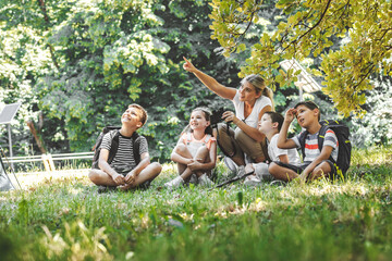 Group of school kids sitting on grass in forest with they teacher.They learning about nature and wildlife.
- 427679804