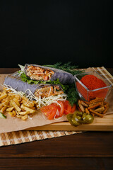 Fresh hot fragrant shawarma cut lies on a wooden board with vegetables, green leaves and fries