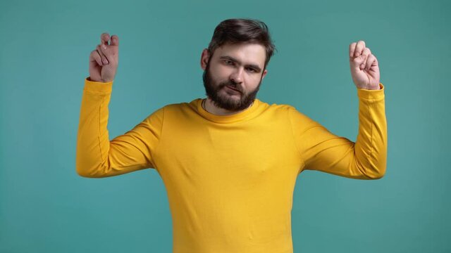 Handsome man showing with hands and two fingers air quotes gesture, bend fingers isolated on blue background. Guy in yellow wear. Not funny, irony and sarcasm concept.
