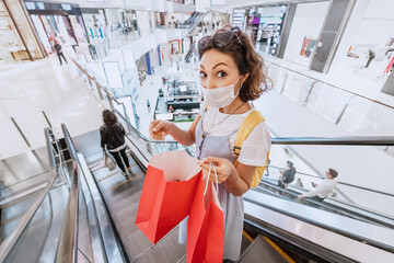 Woman goes shopping and buys new clothes in a mall wearing a face mask during an outbreak and quarantine of a coronavirus infection