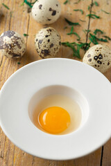Aerial view of quail egg yolk in white plate on wooden table with more eggs, selective focus, vertical