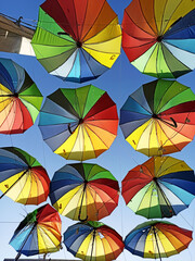 Fototapeta na wymiar many hanging bright rainbow multi-colored umbrellas against the sky, bottom view