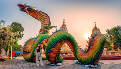 Fototapeta premium Rainbow carve serpent or colorful Thai Naga and asian woman standing in the sunset at Wat Phra That Nong Bua temple