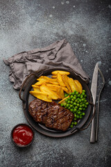 Grilled meat beef steak with potato chips french fries and green peas served with red tomato sauce...