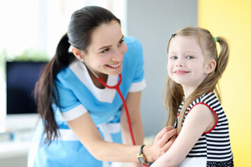 Smiling doctor listens with stethoscope to breathing of little girl
