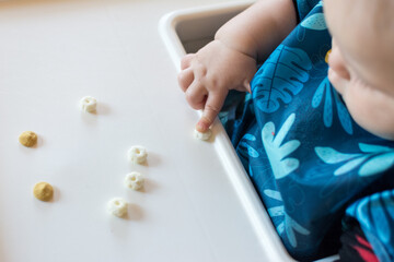 Baby using pointer finger to drag a cereal puff to edge of tray: baby led weaning made fun with smiley face made of cereal puffs