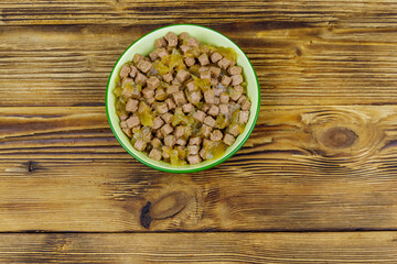 Canned food for cats or dogs in green ceramic bowl on wooden floor. Top view