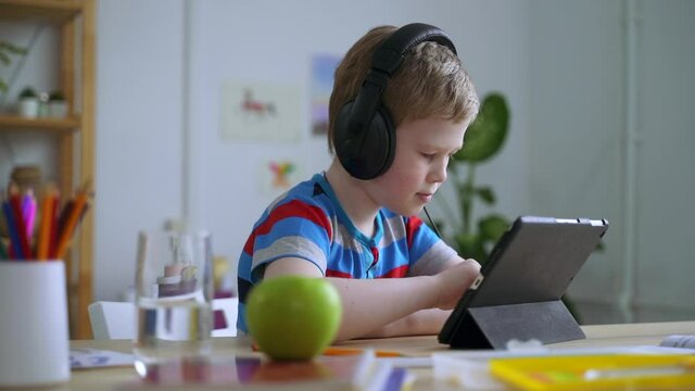 Boy use tablet at desk, wear headphone and read ebook or play game on device Spbas. Preteen kid