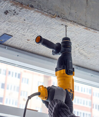male hands of  construction worker drills  hole in concrete with  hand drill. the process of drilling holes in concrete beams and crossbar for various fastenings using  impact drill.