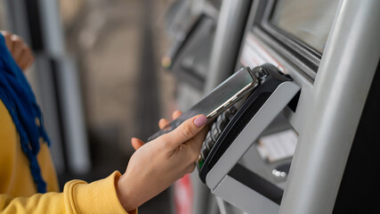 Close-up of a woman paying at a self-service machine using a contactless phone payment