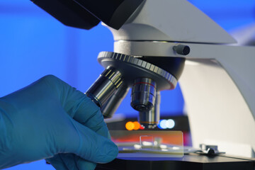 Glass slide with a tissue in hand and a scientific microscope. Screening biopsy sample in medical...