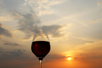 Glass with red wine on sunset background, evening sun and colorful sky are reflected in a glass. Concept of celebration, wine industry