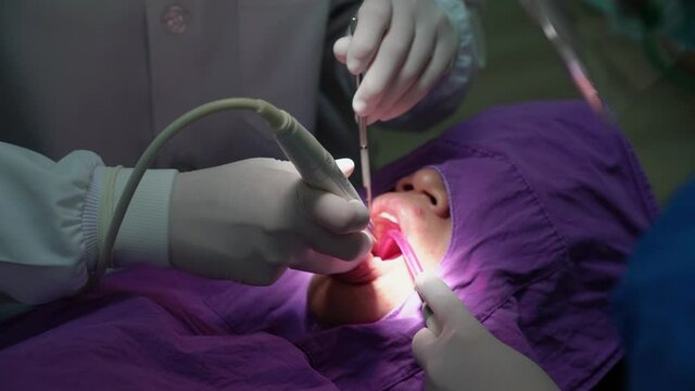 dentist and assistant clean teeth of woman in dental clinic