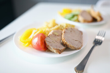 Pieces of fried meat and vegetables lying on white plate closeup