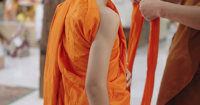 Slow motion of a Buddhist monk is helping a novice who has just passed ordination in the summer during school holidays to dress in a yellow robe.  