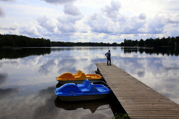 Silhouette of an unrecognizable person on the pier and two colored moored pedal boats, with the...