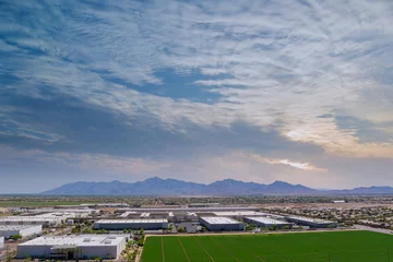 Foto auf Alu-Dibond Aerial panoramic view of goods warehouse logistics center in industrial city zone near of neighbourhood suburban homes in Avondale residential area with among desert the Arizona USA © ungvar
