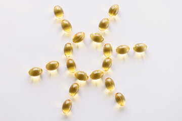 Yellow gel capsules lying in shape of sun on white background closeup