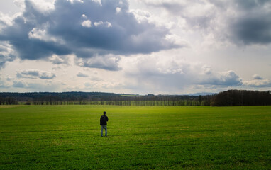 Young caucasian man walking, standing on meadow with dramatic sky. Czech spring landscape