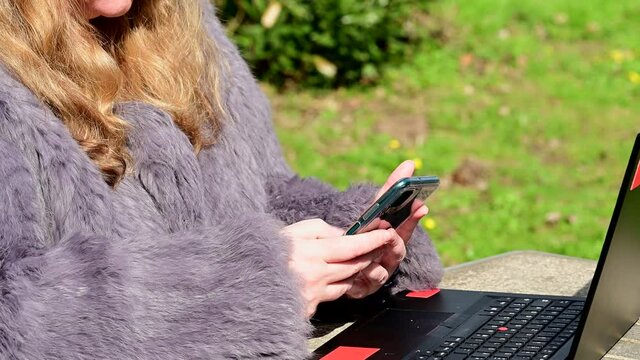 Frau in einer Kaninchenfell Jacke arbeitet im Garten mit einem Notebook im Homeoffice  