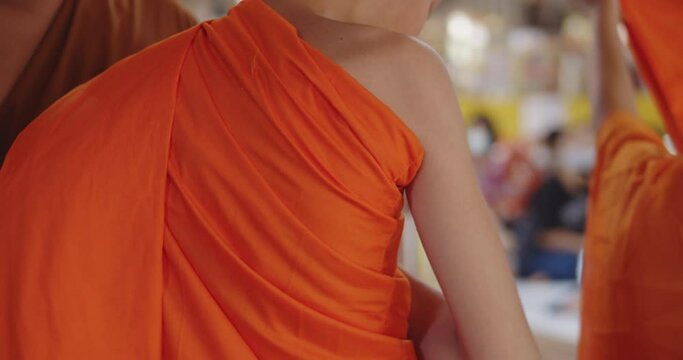 Slow motion of a Buddhist monk is helping a novice who has just passed ordination in the summer during school holidays to dress in a yellow robe.  