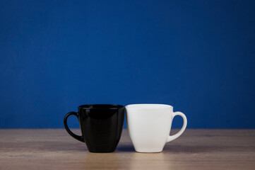Two cups black and white on table against blue wall background
