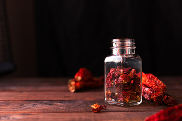 whole pieces of dried pepper lie on a wooden table, and cut pieces of it in a glass jar next to it