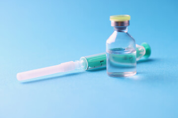 Closeup of glass jar with medicine and sterile syringe on blue background