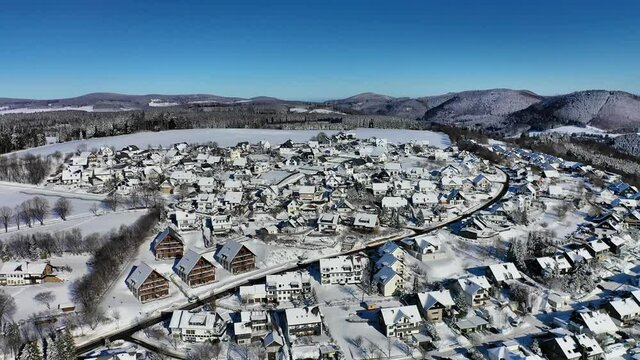 The town of Winterberg in Hochsauerland filmed from the air. The houses of the residential area are located on the snow covered slope. Framed by hills and forest. Flight down.
