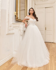 Fototapeta premium Portrait of young beautiful pretty elegant caucasian woman in white fluffy brifal dress standing in bright stylish interior and posing