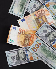 50 euro and 100 usd banknotes are standing side by side on a black background,