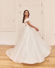 Fototapeta premium Young beauiful happy bride wearing white wedding dress and posing in bright empty interior