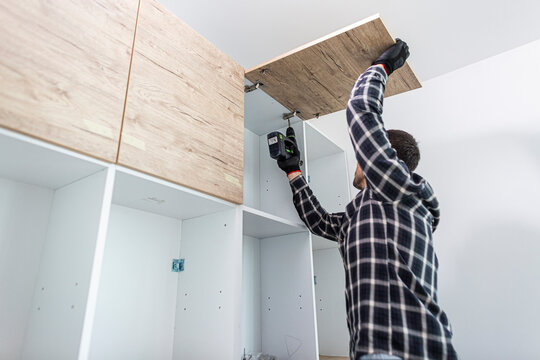 The carpenter sets the door of the kitchen shelves