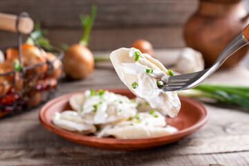 Potato dumplings with sour cream on the wooden table. Varenyky, vareniki, pierogi, pyrohy - dumplings with filling.